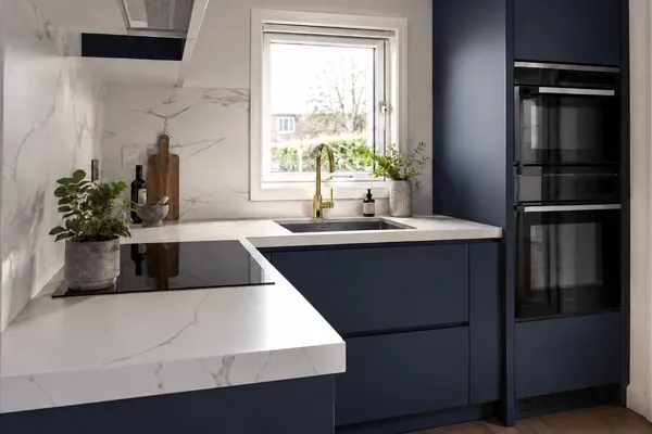 Modern bespoke kitchen in a UK tiny house featuring a 20mm quartz worktop and matte navy custom cabinets.